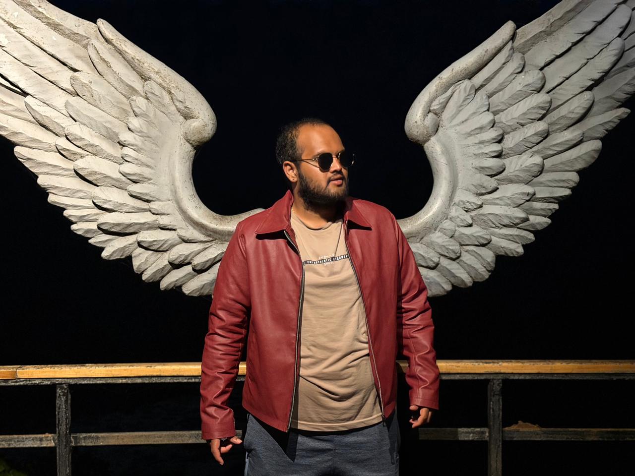 Dhanush P. Soorya in front of a dark wall with sculpted wings.